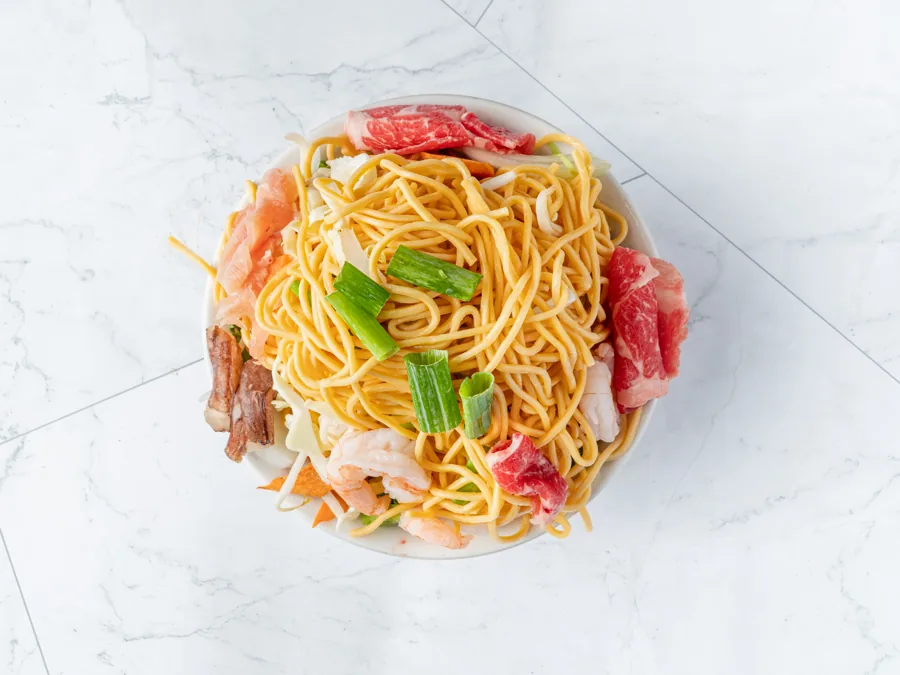 A Mongolian BBQ bowl before grilling: noodles piled with sliced beef, shrimp, mushrooms, cabbage and green onion, seen from above