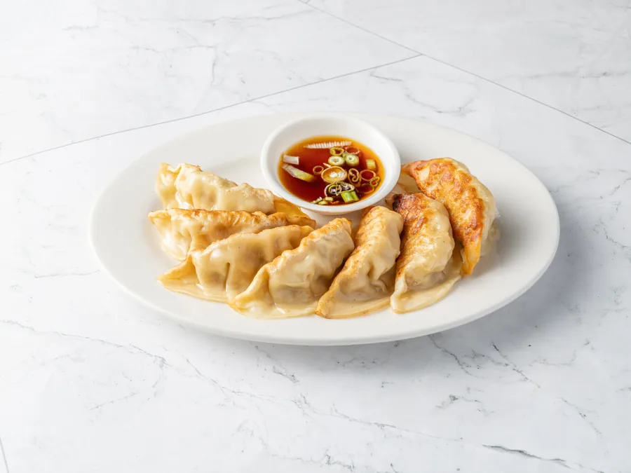 Seven pan-fried pot stickers with a dish of soy dipping sauce