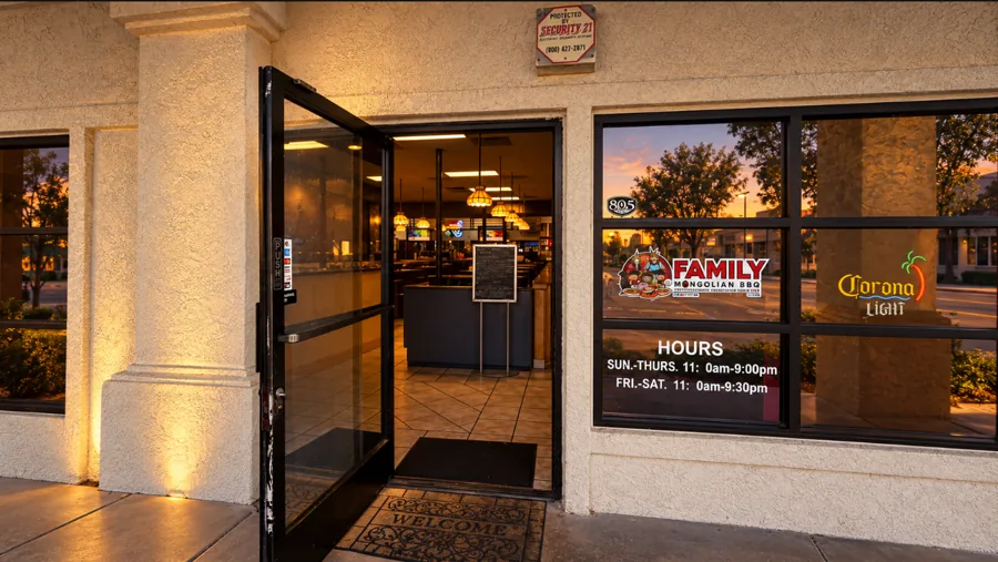 The open front door at evening with warm pendant lights glowing inside and the hours sign in the window