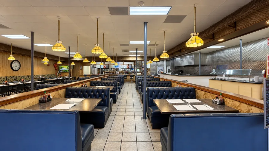 Dining room with rows of navy tufted booths, amber stained-glass pendant lights and the stainless grill station at the back